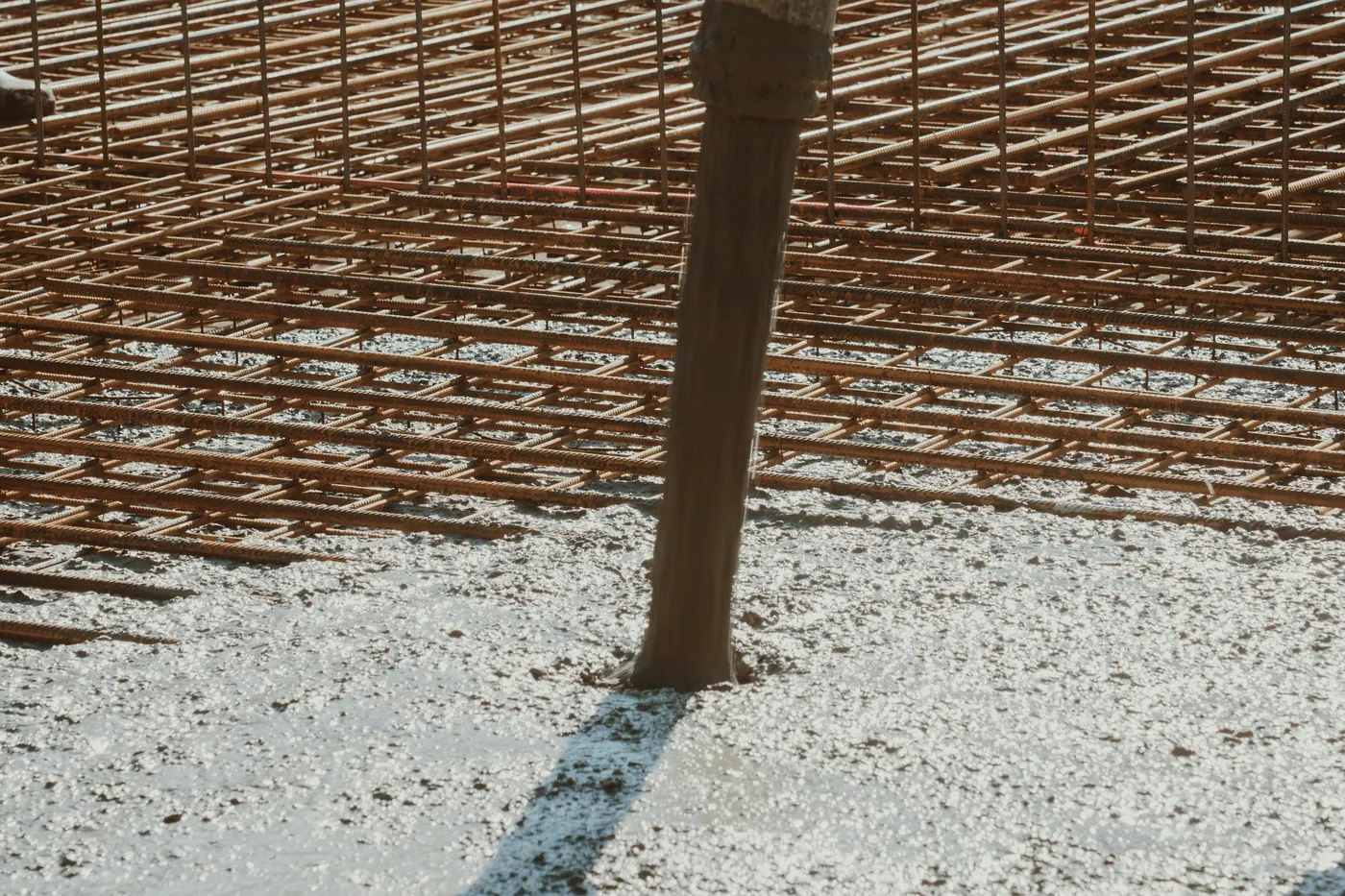 Concrete pouring from a pump hose onto a grid of rusty steel reinforcing bars